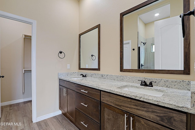 full bath featuring an enclosed shower, double vanity, wood finished floors, and a sink