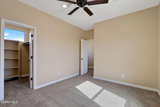 unfurnished bedroom with carpet floors, a spacious closet, baseboards, and a ceiling fan