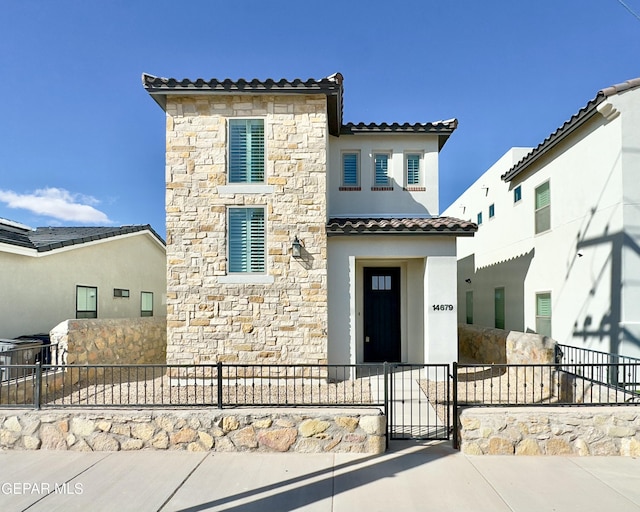 view of front of home featuring a fenced front yard, stone siding, stucco siding, and a tiled roof