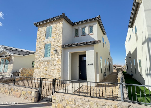 mediterranean / spanish-style home with stone siding, a fenced front yard, and stucco siding