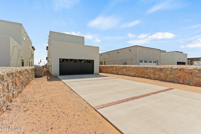 view of side of home with stucco siding, concrete driveway, an outdoor structure, and fence