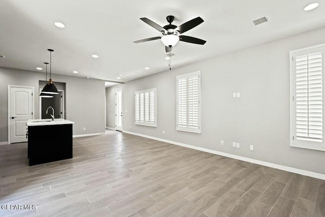 unfurnished living room with a ceiling fan, visible vents, light wood finished floors, and baseboards