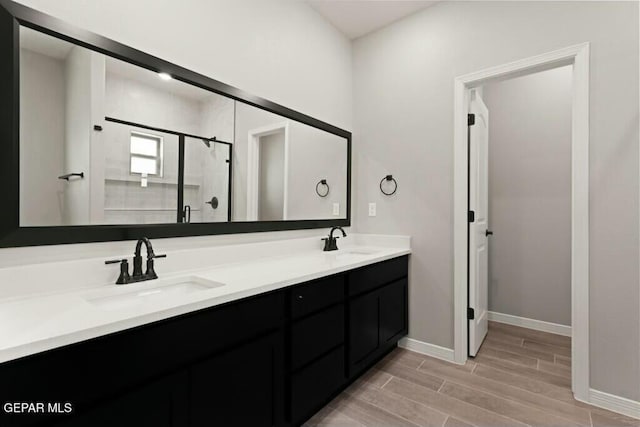 bathroom featuring double vanity, a shower stall, wood finish floors, and a sink