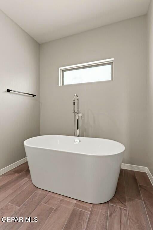 full bath with wood finish floors, baseboards, and a freestanding bath