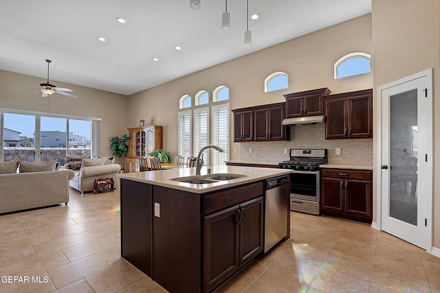 kitchen with under cabinet range hood, stainless steel appliances, a sink, light countertops, and tasteful backsplash