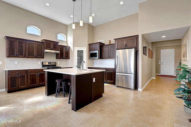 kitchen with appliances with stainless steel finishes, light countertops, dark brown cabinets, under cabinet range hood, and a sink