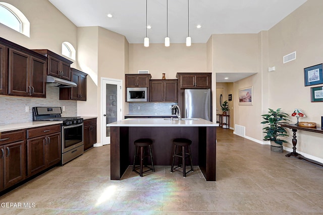 kitchen featuring dark brown cabinetry, under cabinet range hood, a high ceiling, and appliances with stainless steel finishes