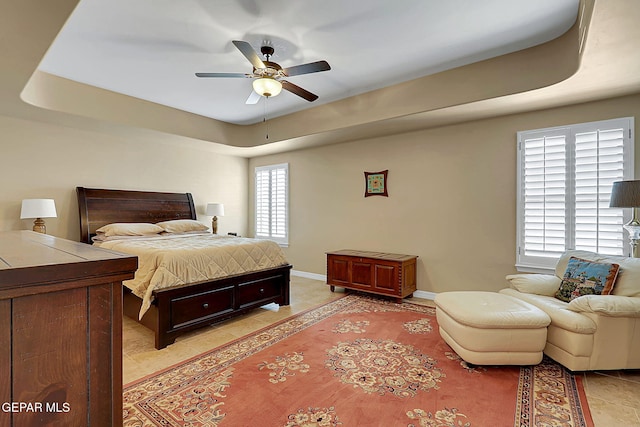 bedroom with light tile patterned floors, a ceiling fan, baseboards, and a tray ceiling