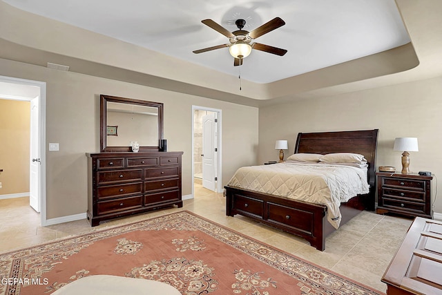 bedroom with a tray ceiling, connected bathroom, baseboards, and light tile patterned floors