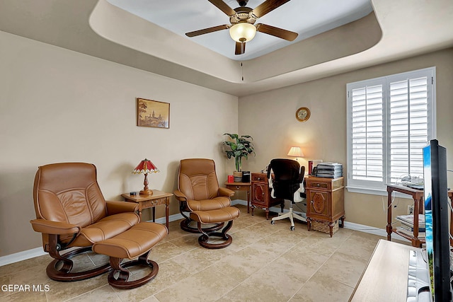 office space with baseboards, a tray ceiling, and ceiling fan