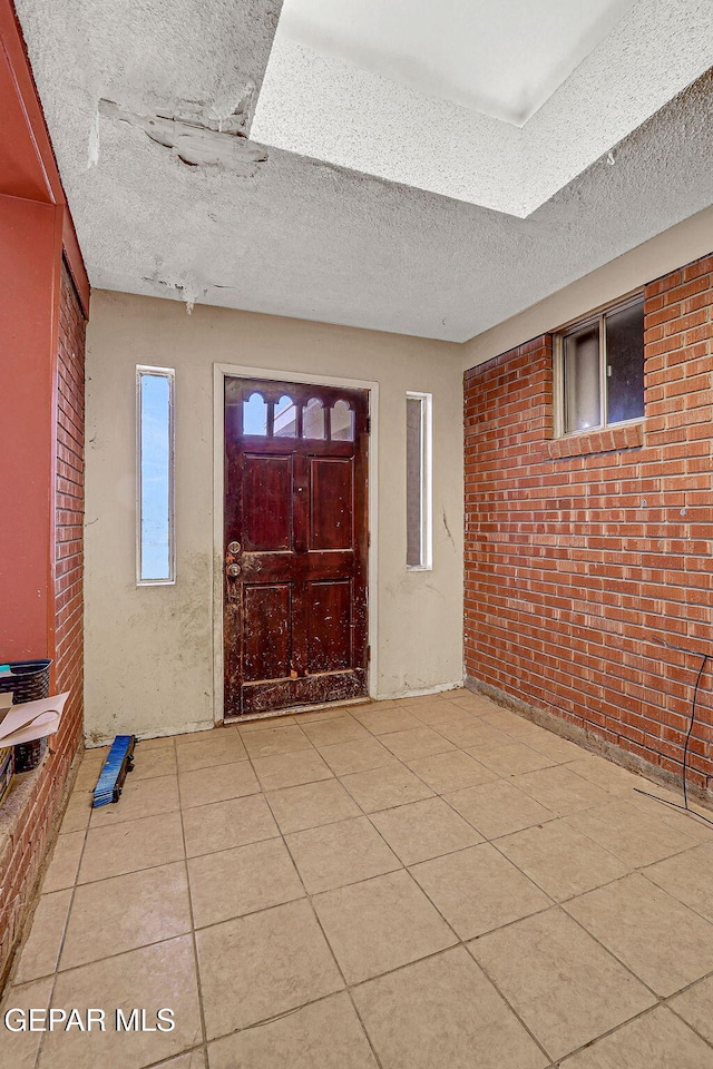 tiled foyer entrance with brick wall and a textured ceiling