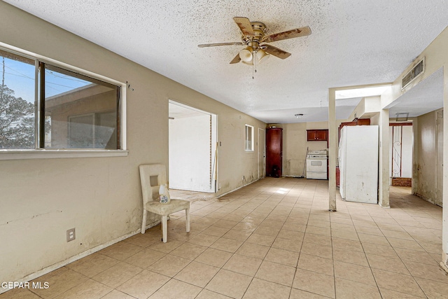 spare room featuring a textured ceiling, light tile patterned flooring, visible vents, and a ceiling fan