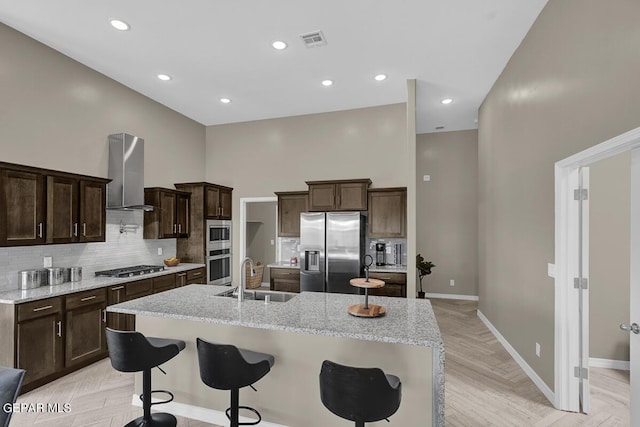 kitchen featuring visible vents, a towering ceiling, island exhaust hood, stainless steel appliances, and a sink