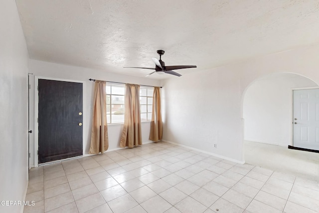 empty room with arched walkways, light tile patterned floors, ceiling fan, a textured ceiling, and baseboards