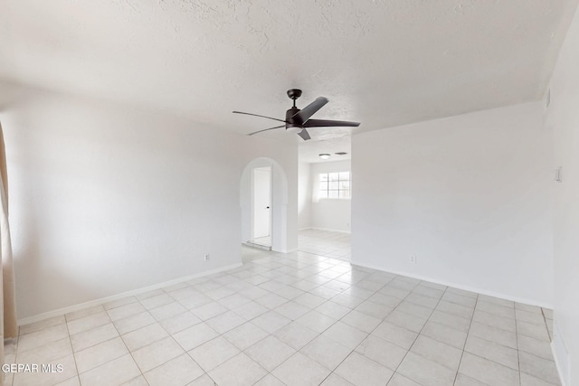 spare room with arched walkways, light tile patterned floors, ceiling fan, a textured ceiling, and baseboards