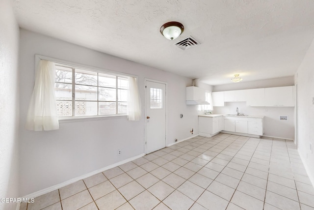 kitchen with a textured ceiling, a sink, visible vents, and white cabinets