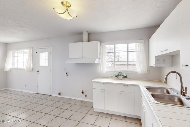 kitchen with light tile patterned floors, plenty of natural light, tile counters, and a sink