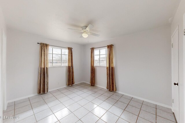 empty room with light tile patterned floors, a ceiling fan, and baseboards