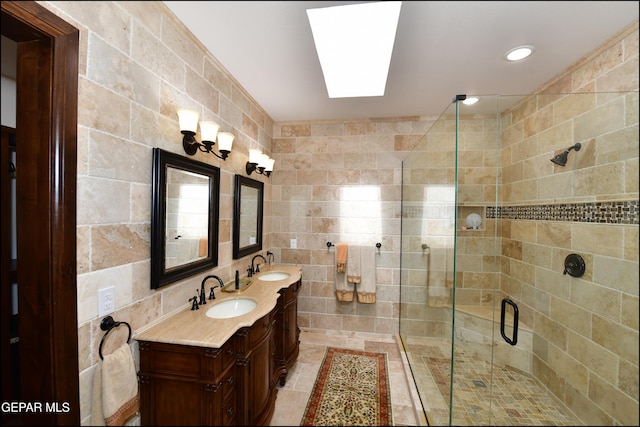 full bath with double vanity, a skylight, a sink, a shower stall, and tile walls