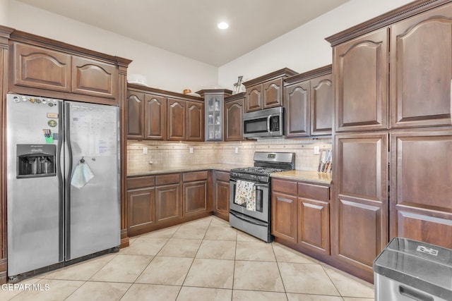 kitchen with appliances with stainless steel finishes, light tile patterned flooring, backsplash, and light stone countertops