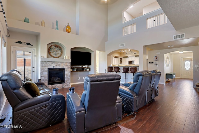 living room featuring dark wood-style flooring, a fireplace, visible vents, and baseboards