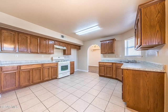 kitchen with brown cabinetry, arched walkways, visible vents, and white gas range oven