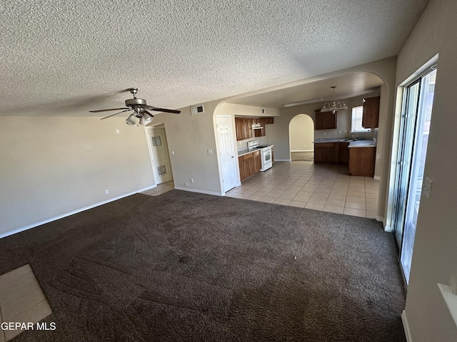 unfurnished living room featuring visible vents, arched walkways, a ceiling fan, carpet, and a textured ceiling