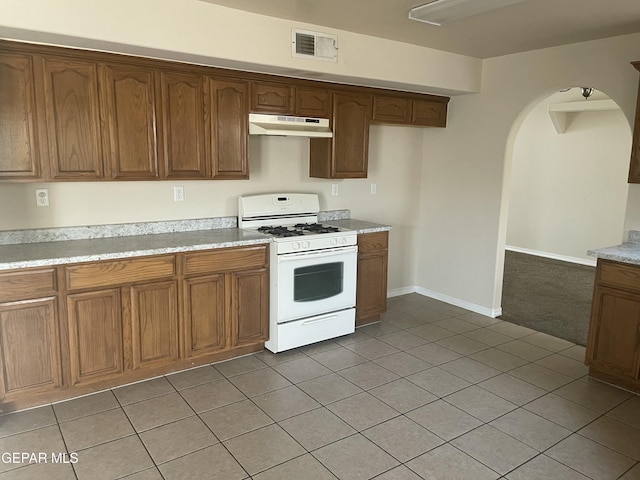 1513 Prickley Pear Dr, El Paso, TX 79912 - kitchen with white gas range oven, under cabinet range hood, arched walkways, light countertops, and light tile patterned floors