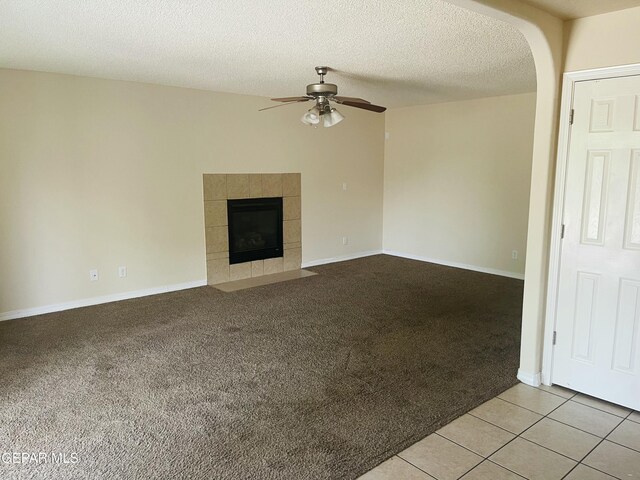 1513 Prickley Pear Dr, El Paso, TX 79912 - unfurnished living room featuring a ceiling fan, light colored carpet, arched walkways, a tiled fireplace, and a textured ceiling