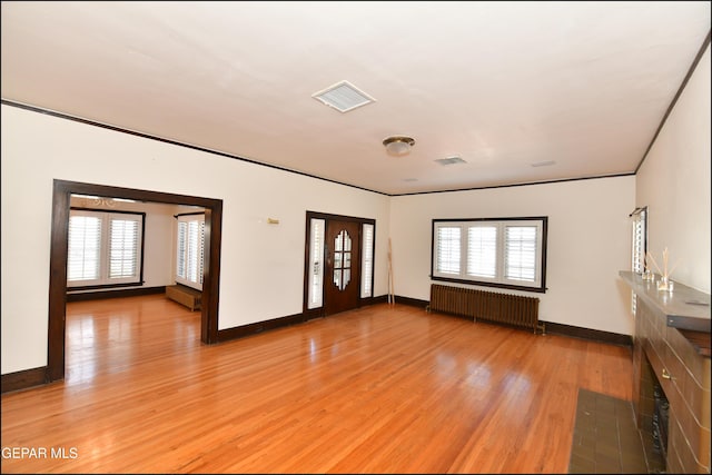 empty room featuring baseboards, visible vents, light wood-style flooring, and radiator heating unit