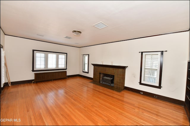 unfurnished living room featuring a fireplace, visible vents, baseboards, light wood-style floors, and radiator heating unit