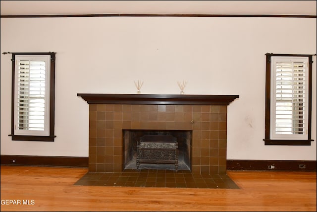 interior details with wood finished floors, a tile fireplace, and baseboards