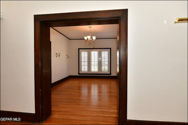 hallway featuring a chandelier, wood finished floors, and baseboards