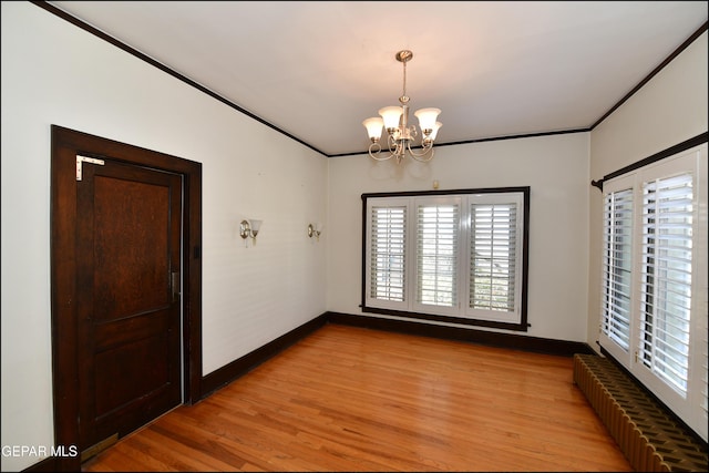 spare room featuring baseboards, light wood finished floors, an inviting chandelier, and crown molding