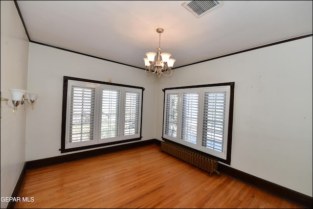 spare room featuring plenty of natural light, visible vents, radiator heating unit, light wood-style flooring, and a chandelier