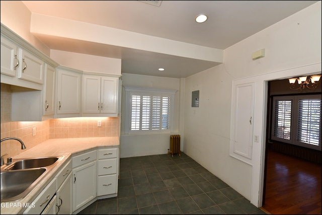 kitchen with tasteful backsplash, radiator heating unit, light countertops, white cabinetry, and a sink