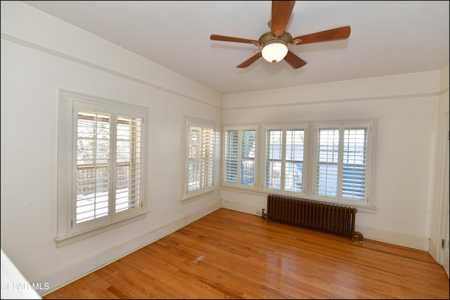 empty room featuring light wood finished floors, radiator heating unit, baseboards, and a ceiling fan