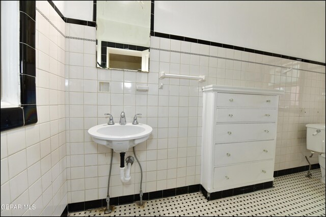 half bathroom with toilet, tile patterned flooring, a sink, and tile walls