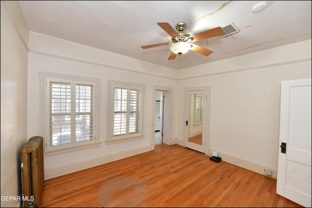 empty room featuring visible vents, baseboards, a ceiling fan, radiator, and light wood-style flooring