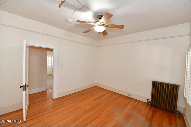 unfurnished room featuring radiator, visible vents, light wood-style floors, a ceiling fan, and baseboards