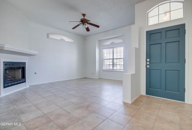 foyer with light tile patterned floors, baseboards, a fireplace, ceiling fan, and a textured ceiling