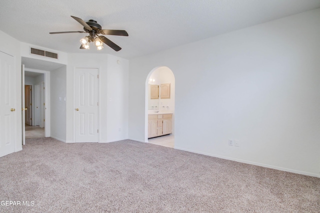 spare room with visible vents, baseboards, light carpet, arched walkways, and a ceiling fan