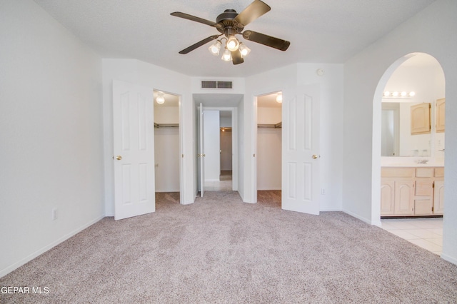 unfurnished bedroom featuring two closets, visible vents, arched walkways, and light colored carpet