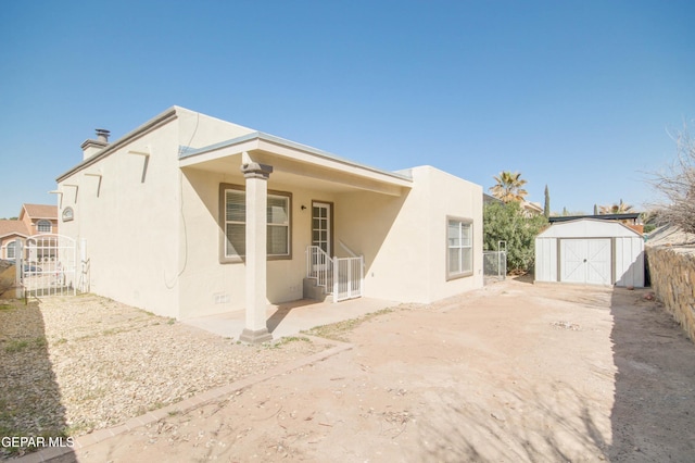 view of front of property featuring stucco siding, driveway, fence, a storage shed, and an outdoor structure