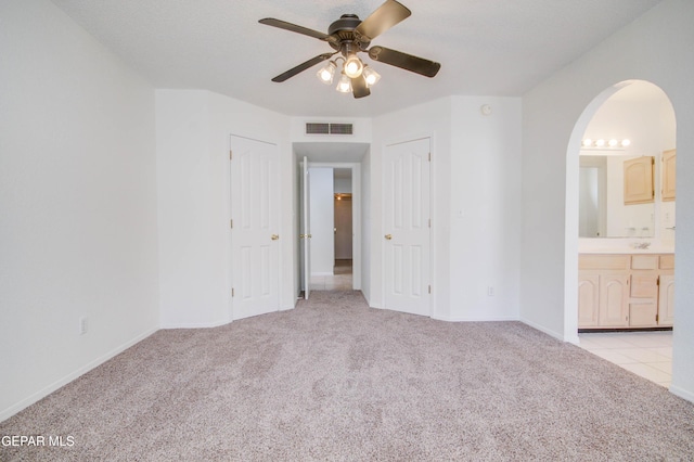 unfurnished bedroom with visible vents, light carpet, ensuite bathroom, arched walkways, and a ceiling fan