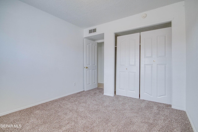 unfurnished bedroom featuring visible vents, a textured ceiling, a closet, carpet flooring, and baseboards