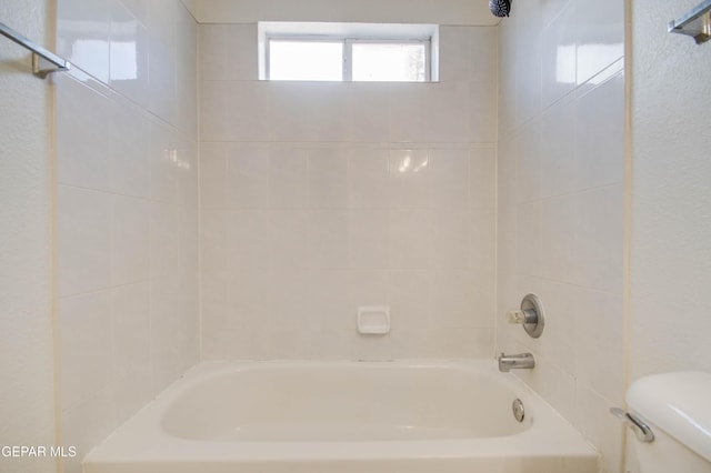 bathroom featuring bathtub / shower combination, toilet, and a textured wall