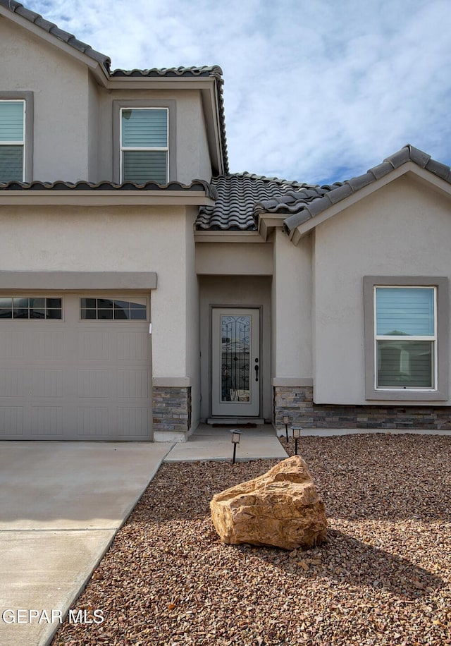 entrance to property with driveway, stone siding, a tiled roof, an attached garage, and stucco siding