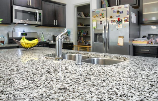 kitchen featuring stainless steel appliances, tasteful backsplash, dark brown cabinetry, and light stone countertops