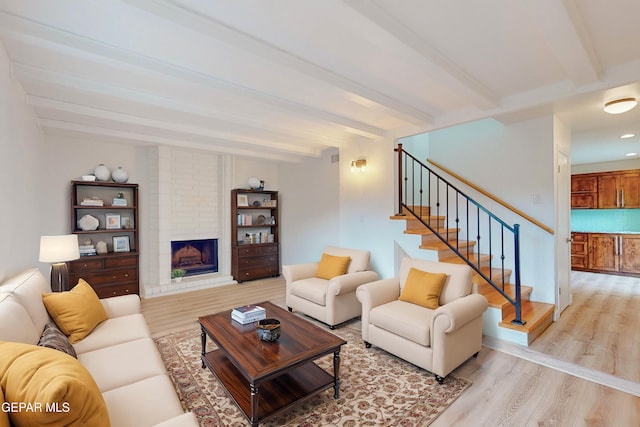 living room with stairs, beamed ceiling, a fireplace, and light wood finished floors